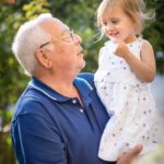 man in blue polo shirt carrying girl in white and pink floral dress