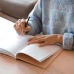 woman in white and gray sweater writing on white paper