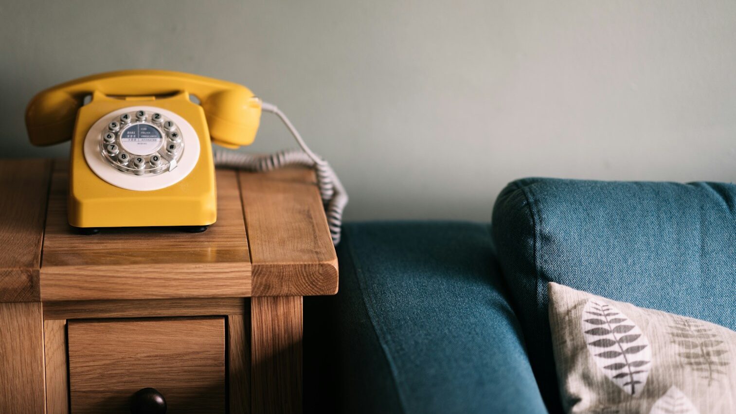 photo of yellow rotary telephone near blue sofa