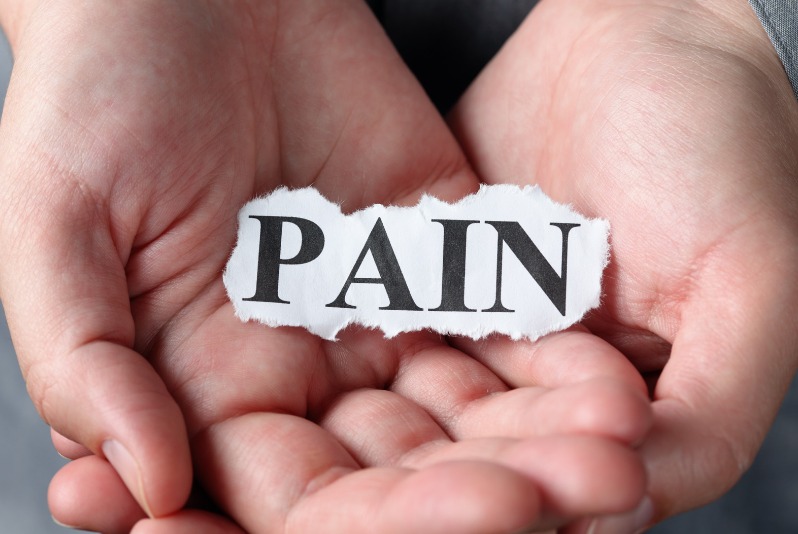 hand holding a piece of paper with the word "pain" printed on it.