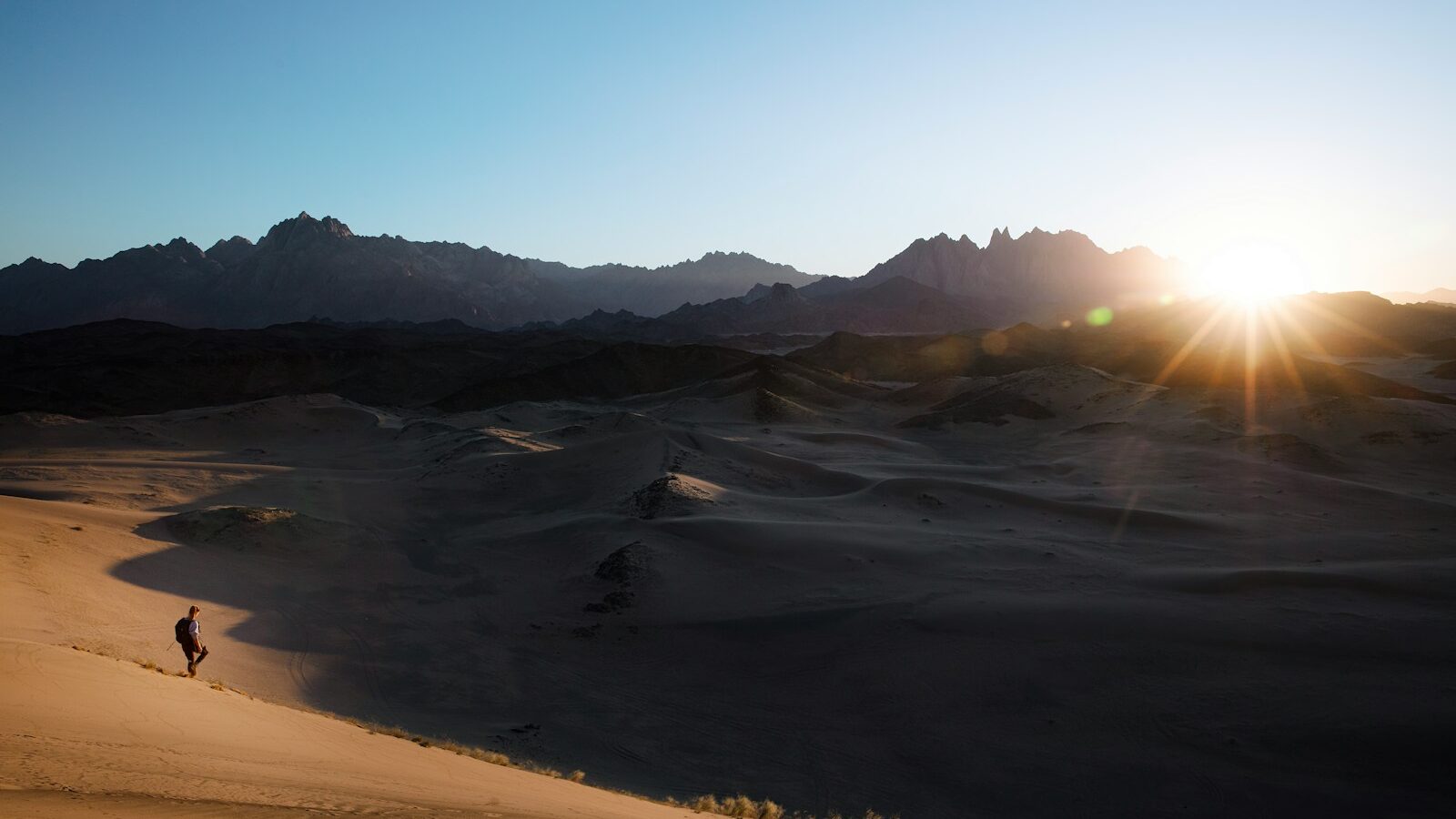 a person is walking in the desert at sunset