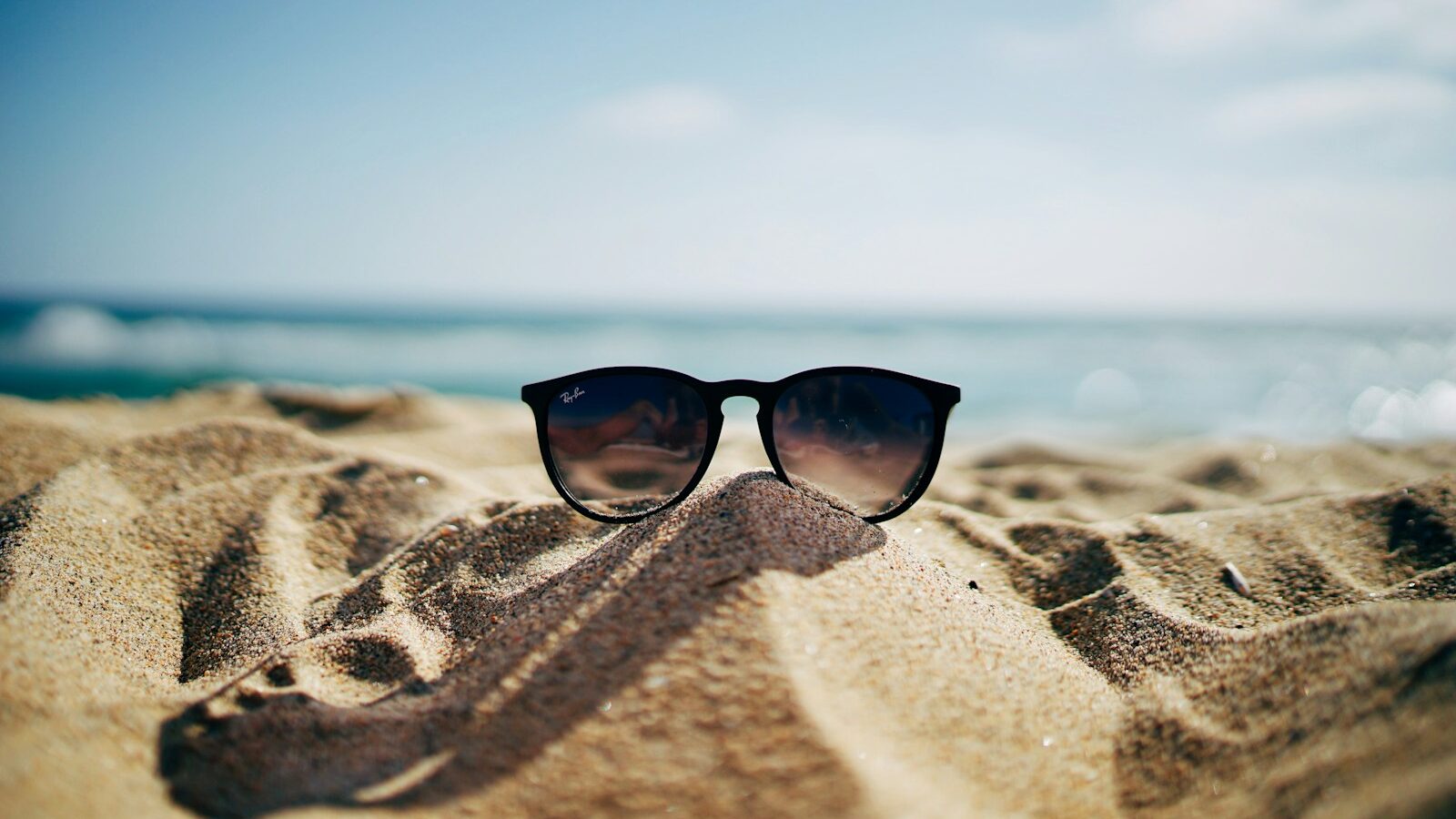 black Ray-Ban Wayfarer sunglasses on beach sand