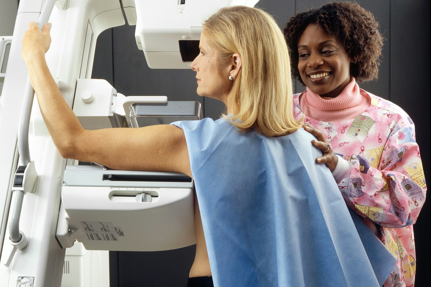 smiling woman standing near another woman beside mammogram machine