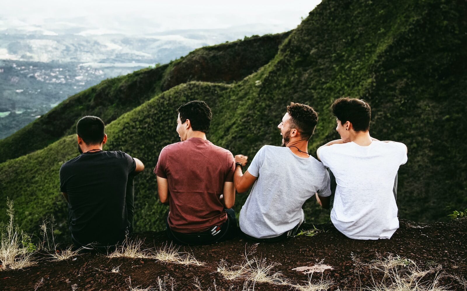 row of four men sitting on mountain trail