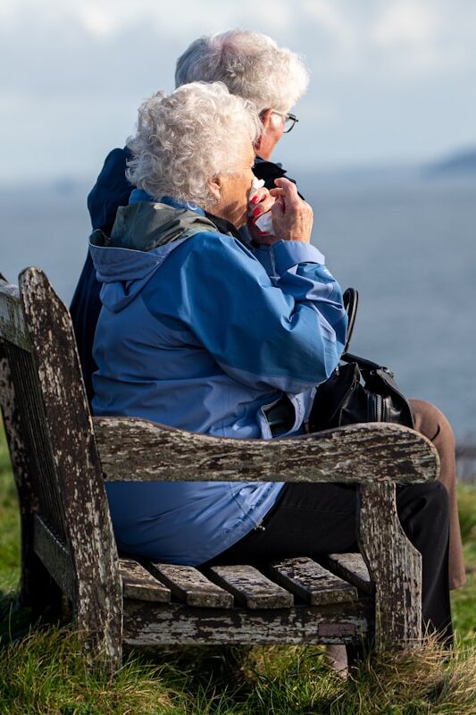 man and woman sitting on gray wooden bench viewing blue sea during daytime