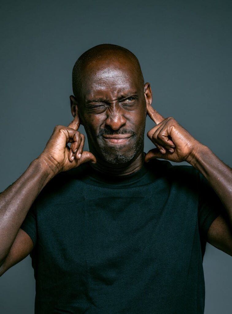 Portrait of a man blocking his ears to avoid loud noise, looking irritated.