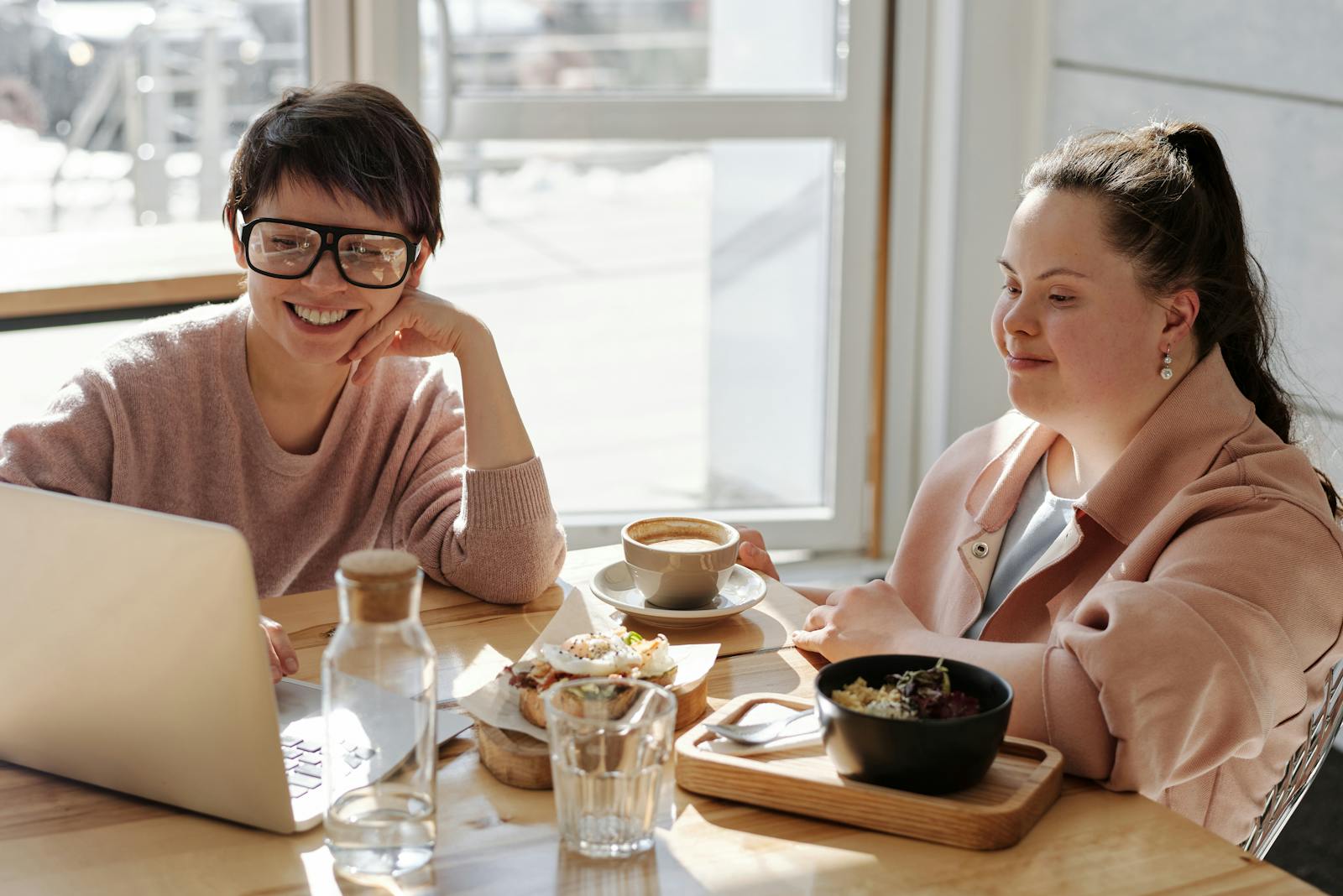 Two cheerful women enjoying coffee and food in a bright, modern indoor setting.
