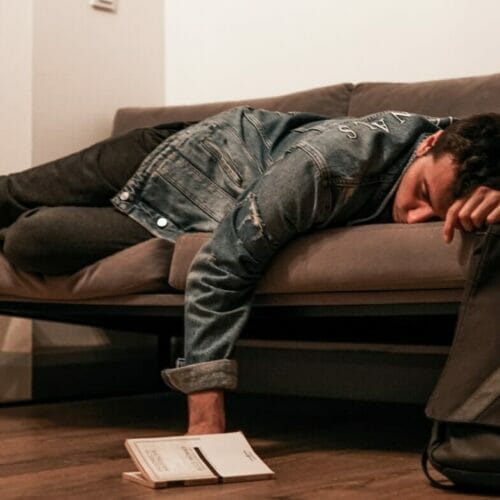 man in black jacket and blue denim jeans lying on brown leather couch