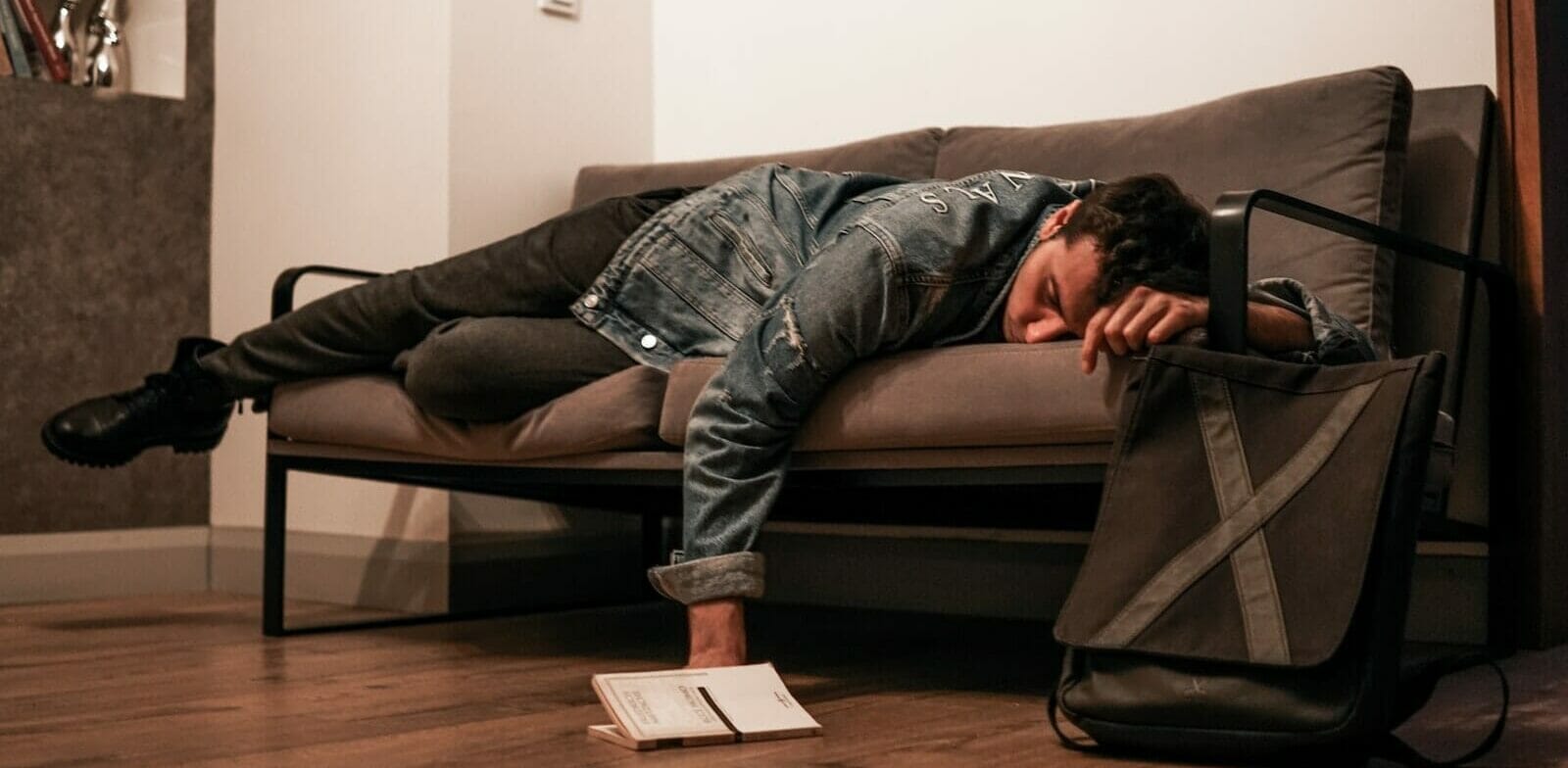 man in black jacket and blue denim jeans lying on brown leather couch