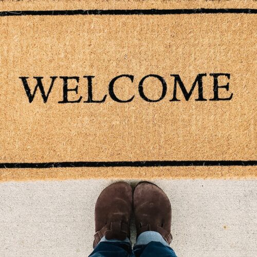 person in blue denim jeans standing on brown and black welcome area rug