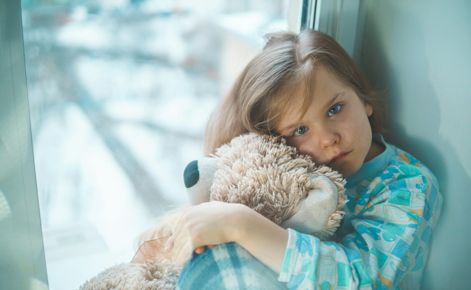 girl in blue white and red plaid shirt hugging brown teddy bear