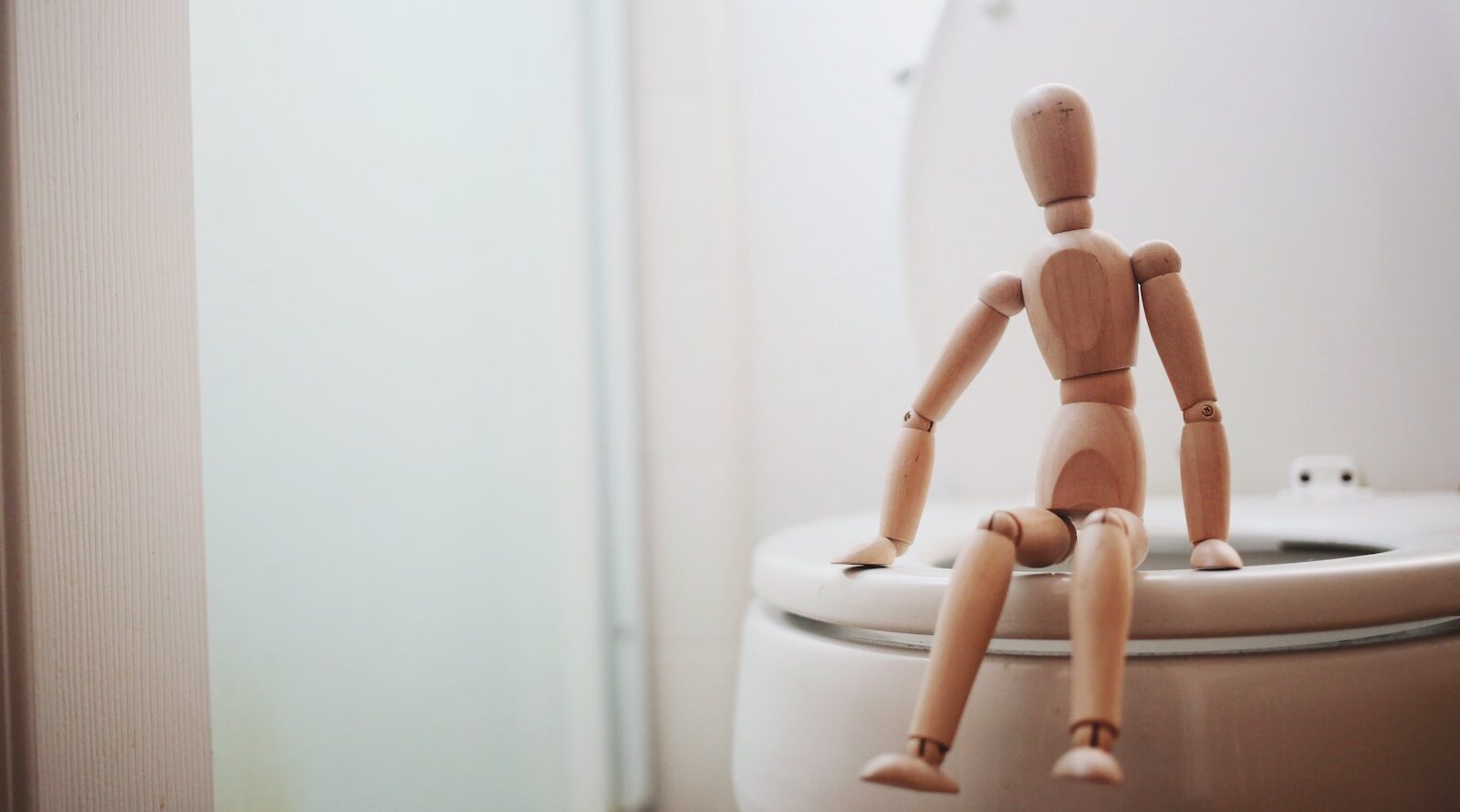 brown wooden doll on white ceramic toilet bowl